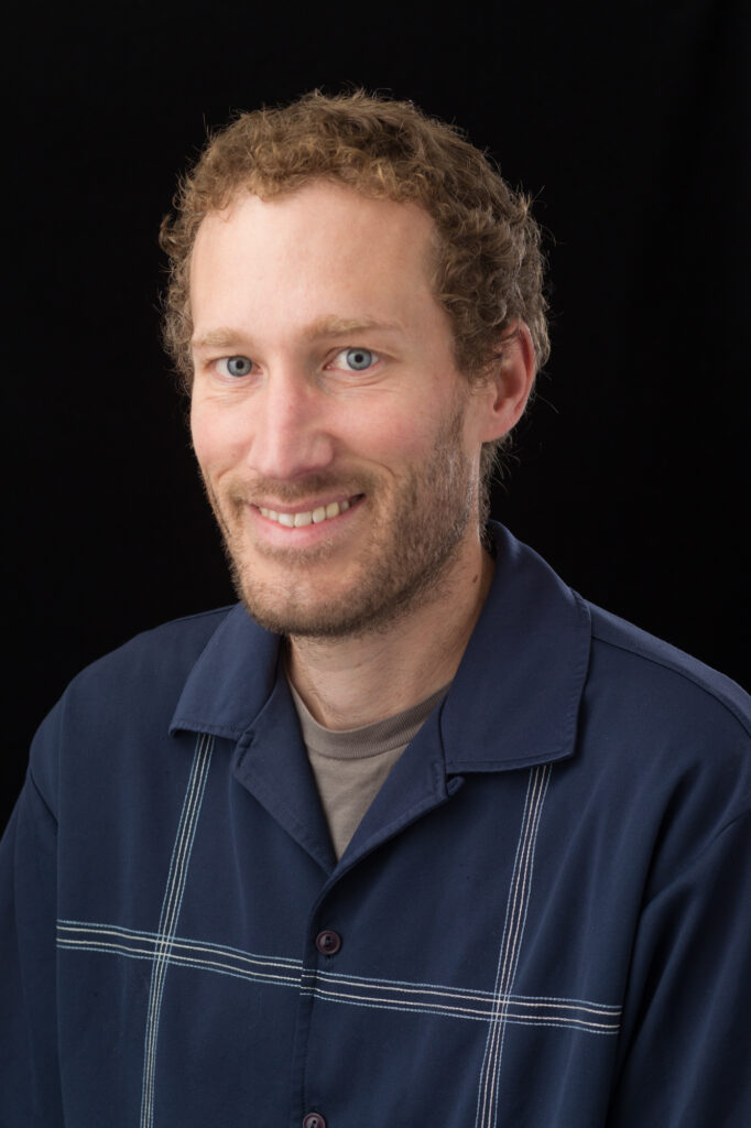 Aaron Gersonde headshot wearing blue stripe shirt in front of a black background
