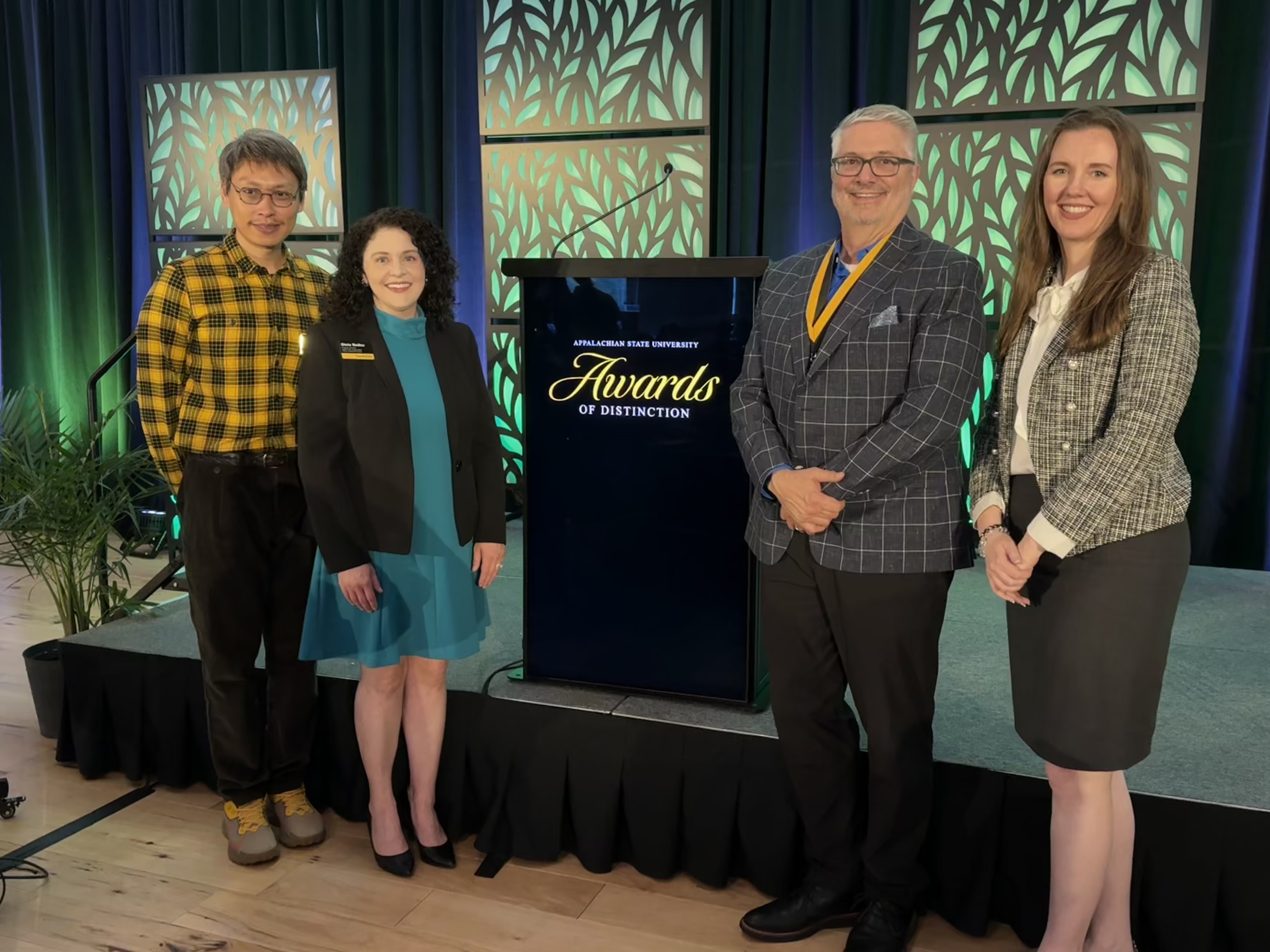 Jim Beeler honored with Staff Excellence Award at campus ceremony. Standing in front of podium with other ORP staff.