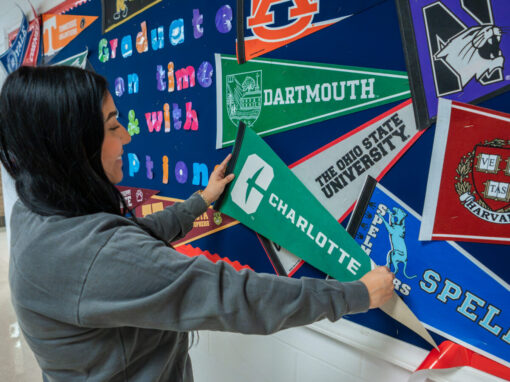 An Advise NC adviser hangs a UNC Charlotte pennant on a bulletin board of other college penants.